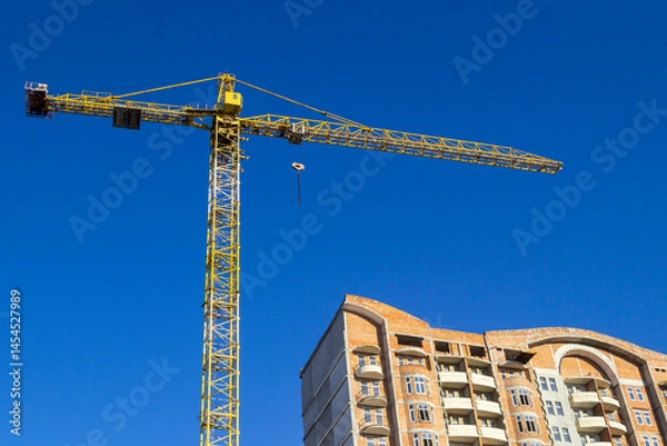 Fototapeta An unfinished building and a construction crane against the background of a sky.