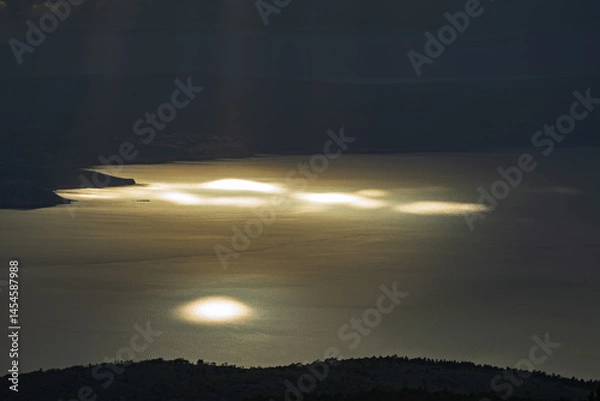 Fototapeta Sunlight falls through the clouds and is reflected in the waters of the Adriatic.