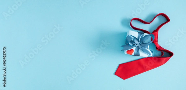 Fototapeta Happy Fathers Day background. Flat lay, top view of red heart shaped necktie, gift box and red heart on blue background.