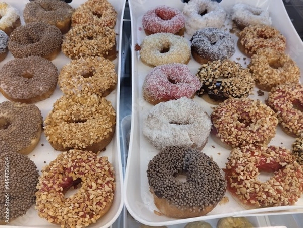 Obraz Donuts in colored glaze in chocolate with sprinkles of nuts puffed rice are on a tray. Virina Ponchikova. Takeaway