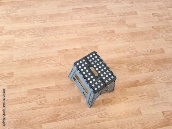 Obraz A foldable step stool with a dotted surface sits on a wooden floor, providing a practical solution for reaching high places in home or office settings.