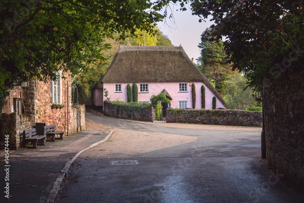 Fototapeta A large classic Devonian house with a thatched roof with the village of Cockington. Location near Torquay. Devon. England
