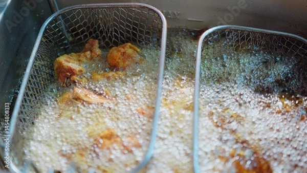 Obraz Close-up of crispy fried chicken pieces sizzling in hot oil inside a deep fryer in a Restaurant, showcasing delicious cooking in a kitchen.