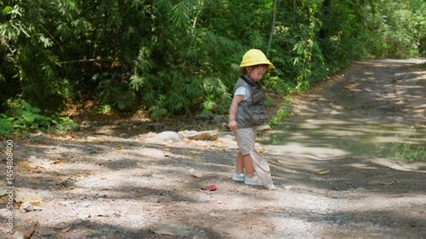 Fototapeta A cheerful Asian child girl with a butterfly net enjoys a sunny day in the forest, ready for an adventure Exploring in nature.