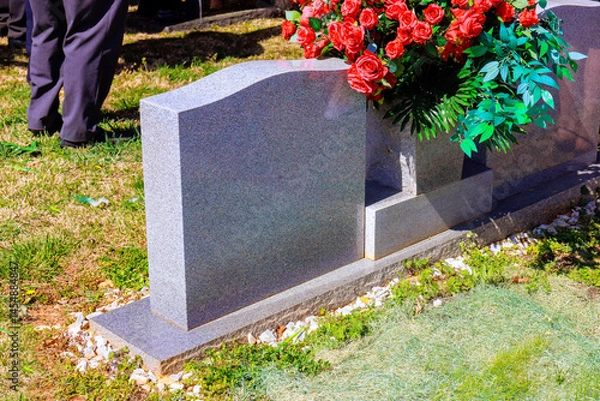 Obraz Attendees gather around gravestone adorned with flowers, honoring loved one in peaceful cemetery.
