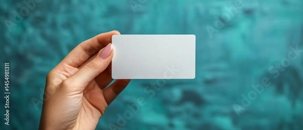 Fototapeta Caucasian hand holds blank business card, presenting it against an aqua textured background.