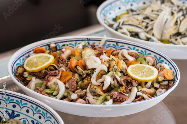 Fototapeta Insalata di Mare, Italian Seafood Salad in a ceramic plate. Italy's classic light, bright salad of gently cooked and marinated seafood with lemon juice, olive oil, parsley, and subtle spices