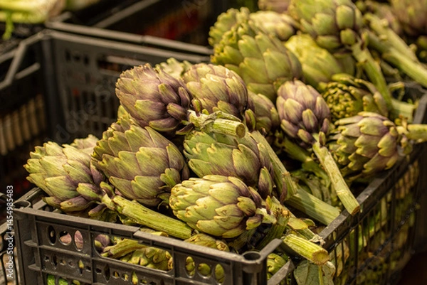 Fototapeta Fresh green artichokes with green leaves displayed on a counter in a street food market, close up