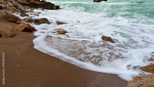 Fototapeta Experience the serene beach waves gently flowing over the rugged rocky shoreline beautifully