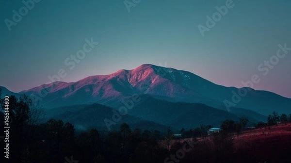 Fototapeta   A stunning image of a mountain range with a cozy house in the foreground and lush trees basking in the warm glow of sunset