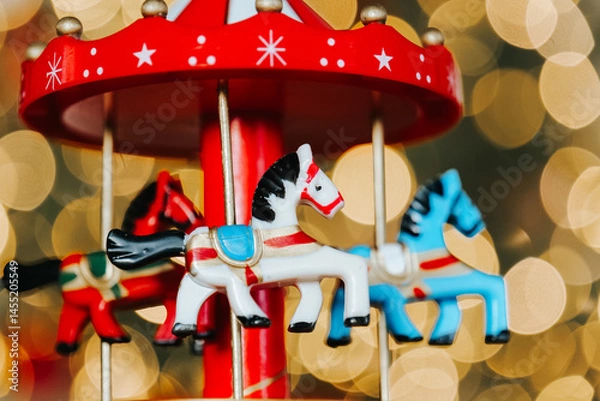 Fototapeta Wooden Christmas carousel horses on garland lights background.Colorful Carousel Ornament with Toy Horses. Red carousel with red, blue and white horse figures close-up. 