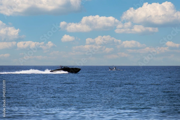 Fototapeta black ocean speedboat passing old fishing boat with sky and clouds