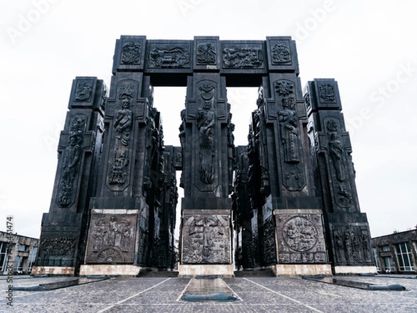 Fototapeta Chronicles of Georgia, monument with black massive 16 pillars Approx, famous tourist attraction, located on Keeni hill near the Tbilisi sea, Georgia, with white fog sky after rain day.