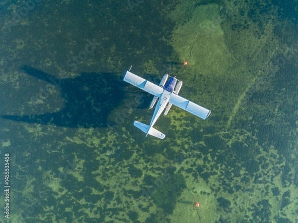 Fototapeta Aerial view of a seaplane, a single-engine aircraft with floats, parked in shallow water near buoys. The plane is stationary, possibly for maintenance or a break. USA.