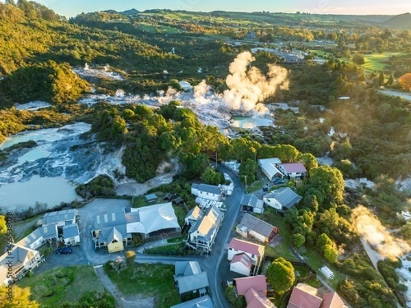 Fototapeta Aerial view of Whakarewarewa Thermal Village, Rotorua, New Zealand. Steam rises from geothermal pools, a natural wonder attracting tourists. Houses are nestled near the park.