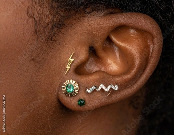 Fototapeta Closeup of Woman's Ear with Multiple Gold and Emerald Piercings
