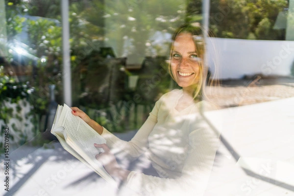 Obraz Young woman smiling by the window reading a book