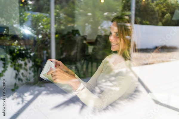 Obraz Woman reading a book by the window at home feeling happy smiling
