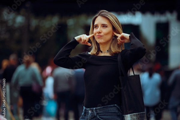Fototapeta Woman Covers her Ears at a Concert Disliking the Music. Unhappy girl blocks out noise at a public event 