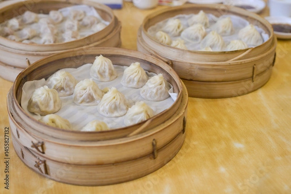 Fototapeta Steaming hot xiao long bao soup dumplings in traditional bamboo baskets on a wooden table, Asian cuisine.