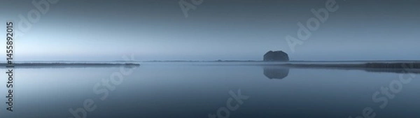 Obraz Misty lake scene with a small island, calm water reflecting the sky