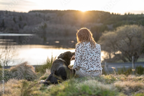 Fototapeta Une fille et son chien qui regarde le coucher de soleil au bord d'un lac