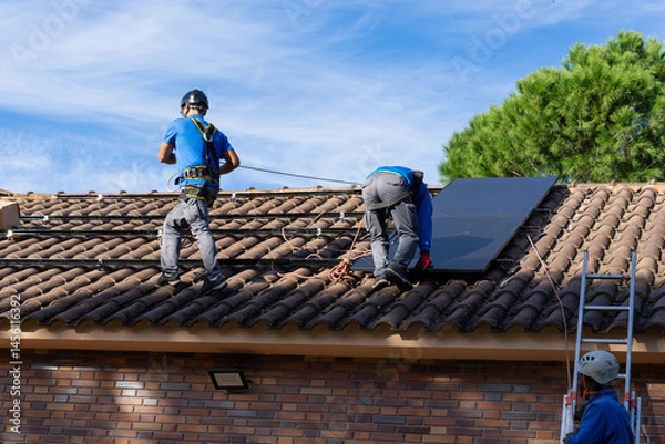 Fototapeta Workers installing solar panel on a roof of residential building