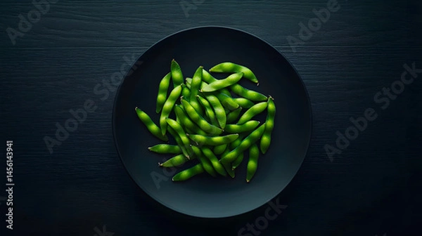 Fototapeta A plate of green beans is on a black table