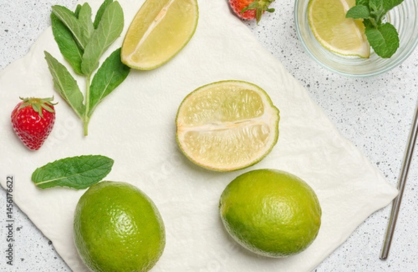 Fototapeta A top down view of ingredients for a refreshing drink, including whole and sliced limes, fresh mint sprigs, empty glass, metal straw