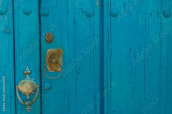Fototapeta Weathered blue painted wooden door featuring a metal handle and knocker, showcasing a rustic and vintage architectural style