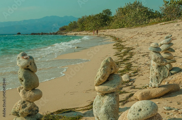 Fototapeta Stone cairns stand on a sandy beach, providing a tranquil contrast to the gentle waves and distant mountains