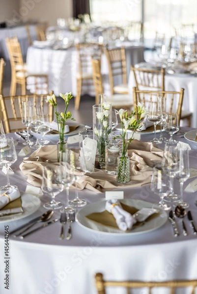 Fototapeta A wedding table covered with a white tablecloth, decorated with flowers, candles, glasses and cutlery