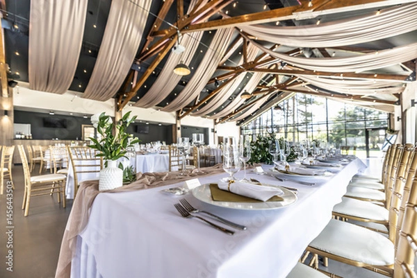 Fototapeta Wedding setting and decorated tables in a beautiful modern interior of a performance hall with a modern light ceiling of wooden construction