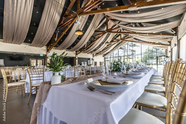 Fototapeta Wedding setting and decorated tables in a beautiful modern interior of a performance hall with a modern light ceiling of wooden construction