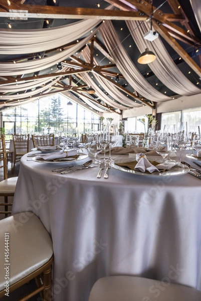 Fototapeta Wedding setting and decorated tables in a beautiful modern interior of a performance hall with a modern light ceiling of wooden construction