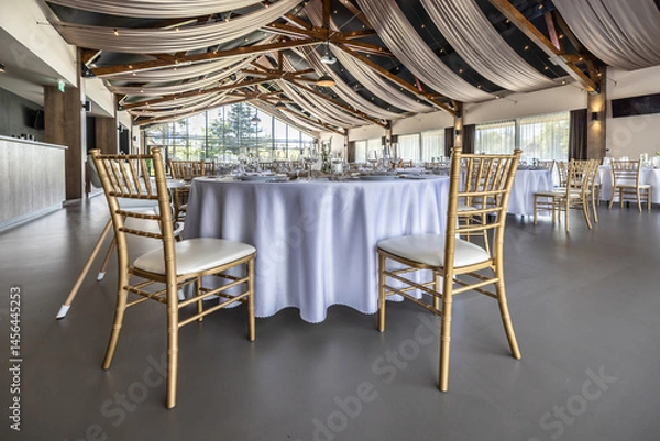Fototapeta Wedding setting and decorated tables in a beautiful modern interior of a performance hall with a modern light ceiling of wooden construction