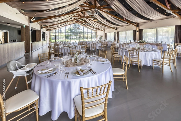 Fototapeta Wedding setting and decorated tables in a beautiful modern interior of a performance hall with a modern light ceiling of wooden construction
