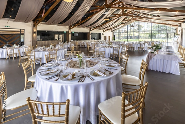 Fototapeta Wedding setting and decorated tables in a beautiful modern interior of a performance hall with a modern light ceiling of wooden construction