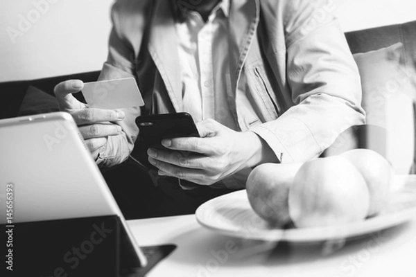 Fototapeta hipster hand using smart phone,digital tablet docking keyboard,holding cradit card payments online business,sitting on sofa in living room,work at home concept,black and white
