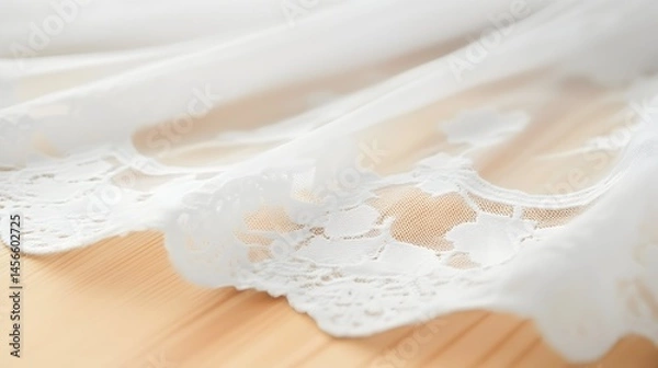 Fototapeta Delicate white lace trim adorns sheer fabric, resting on light wood.  Intricate floral patterns highlight the craftsmanship
