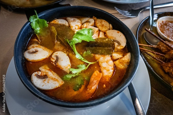 Fototapeta Tom Yam Khung, spicy Thai soup with shrimps and mushrooms, at a restaurant, garnished with cilantro