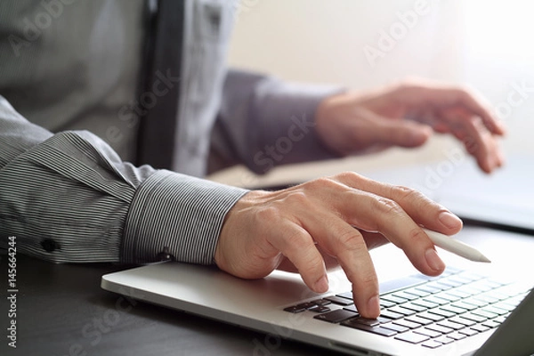 Fototapeta close up of businessman working with mobile phone and stylus pen and laptop computer  on wooden desk in modern office