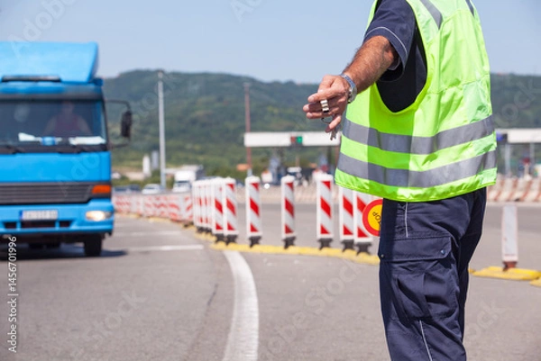 Fototapeta Highway traffic police officer wearing a reflective vest signals a blue truck to stop at a checkpoint during daytime road inspection