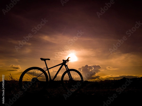 Fototapeta Silhouette Bike Ride: An adventurous bicycle is silhouetted against a dramatic, sunlit sky at dusk, painting a vivid picture of freedom, exploration, and the open road.