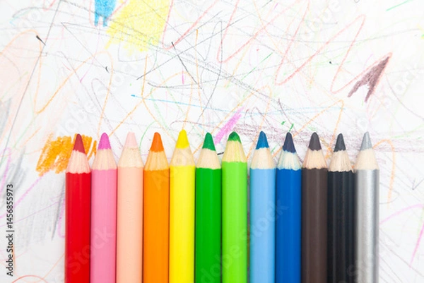 Obraz Multi-colored pencils lie on white paper drawn with multi-colored curved lines.
