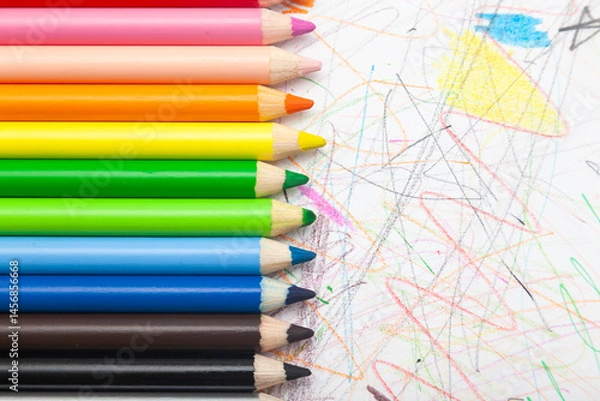 Obraz Multi-colored pencils lie on white paper drawn with multi-colored curved lines.