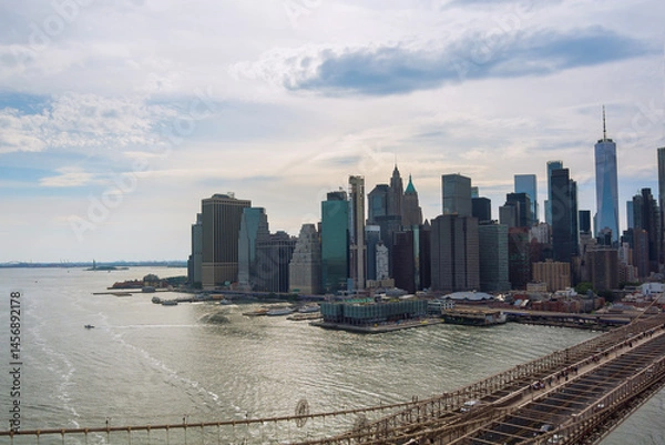 Obraz Cloudy day showcases New York City Manhattan skyline waterfront, with boats gliding through tranquil waters.