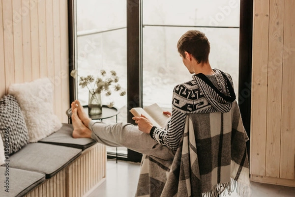 Fototapeta Man Reading Book in Log Cabin in Winter