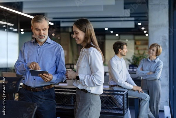 Obraz Two business people discussing work together using a tablet in a modern office