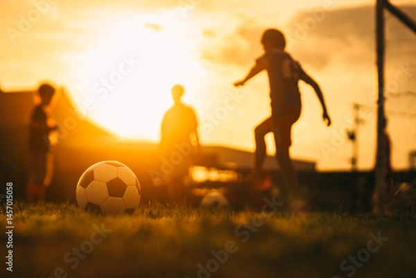 Fototapeta Action sport outdoors of kids having fun playing soccer football for exercise in community rural area under the twilight sunset sky.